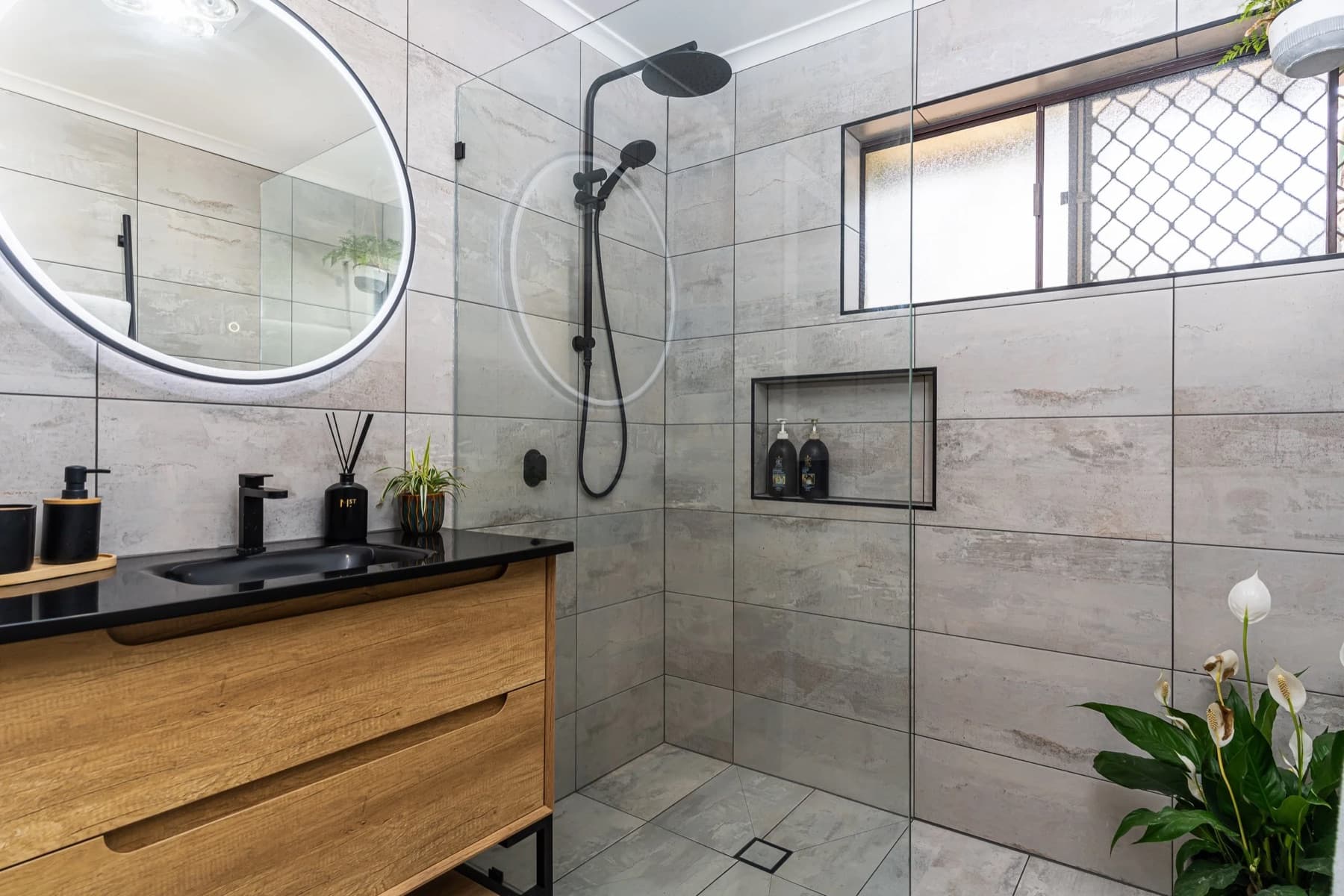 A completed JAYMA Projects Brisbane bathroom with soft daylight, warm stone tile and brushed-gold tapware.